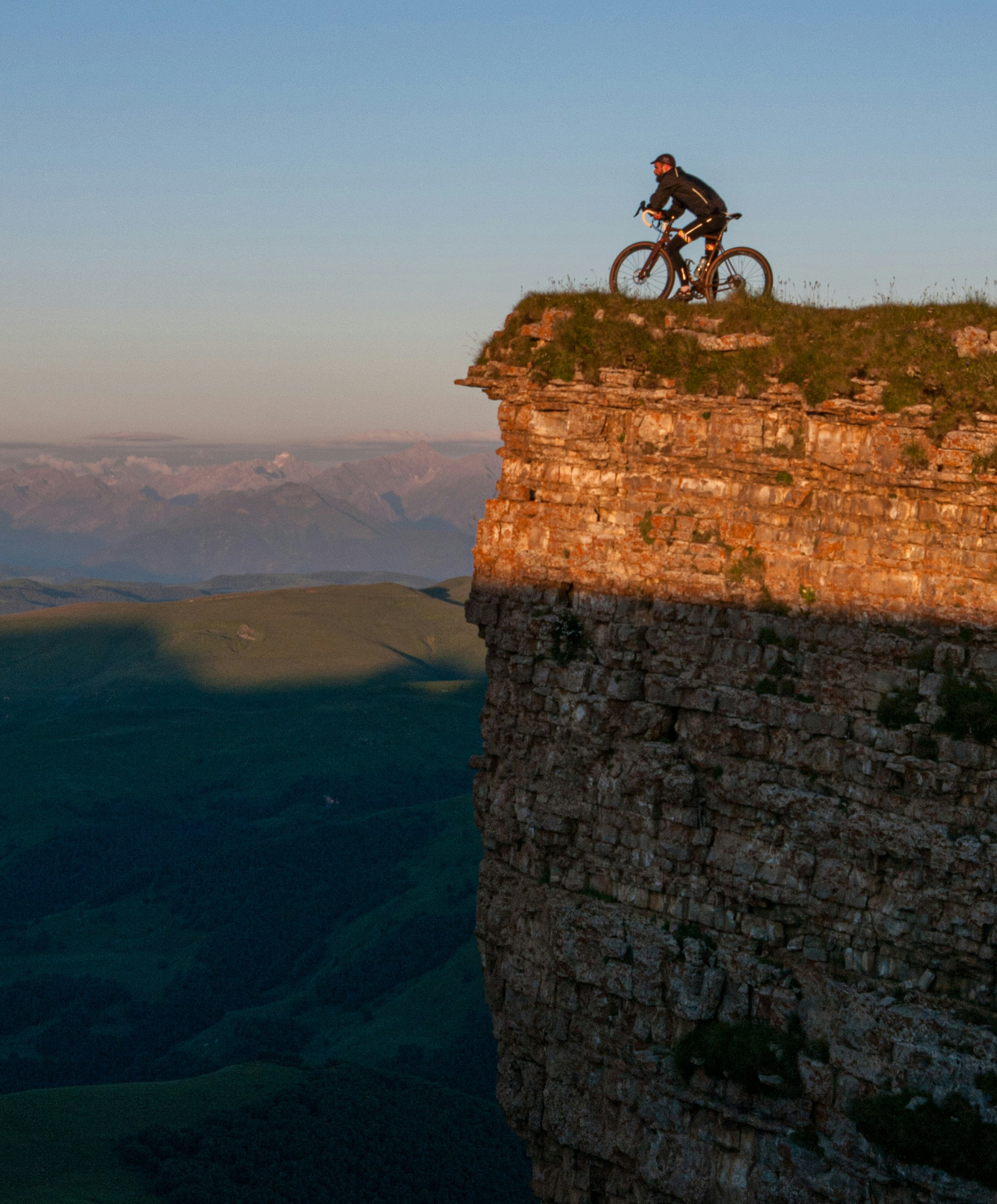 Cyclist on a cliff edge overlooking mountains at golden hour
